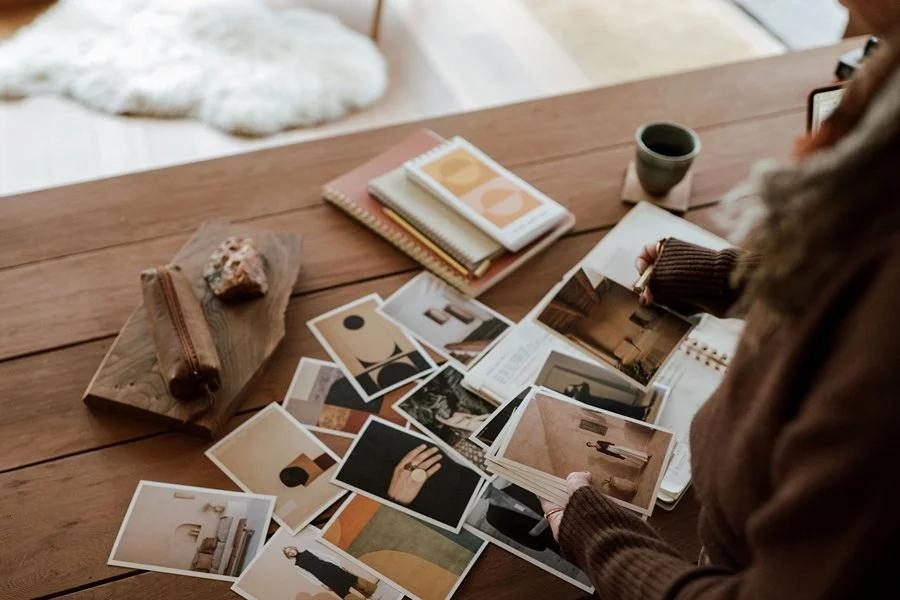 Hands laying out printed images and cards on a wooden table, arranging a set of visuals