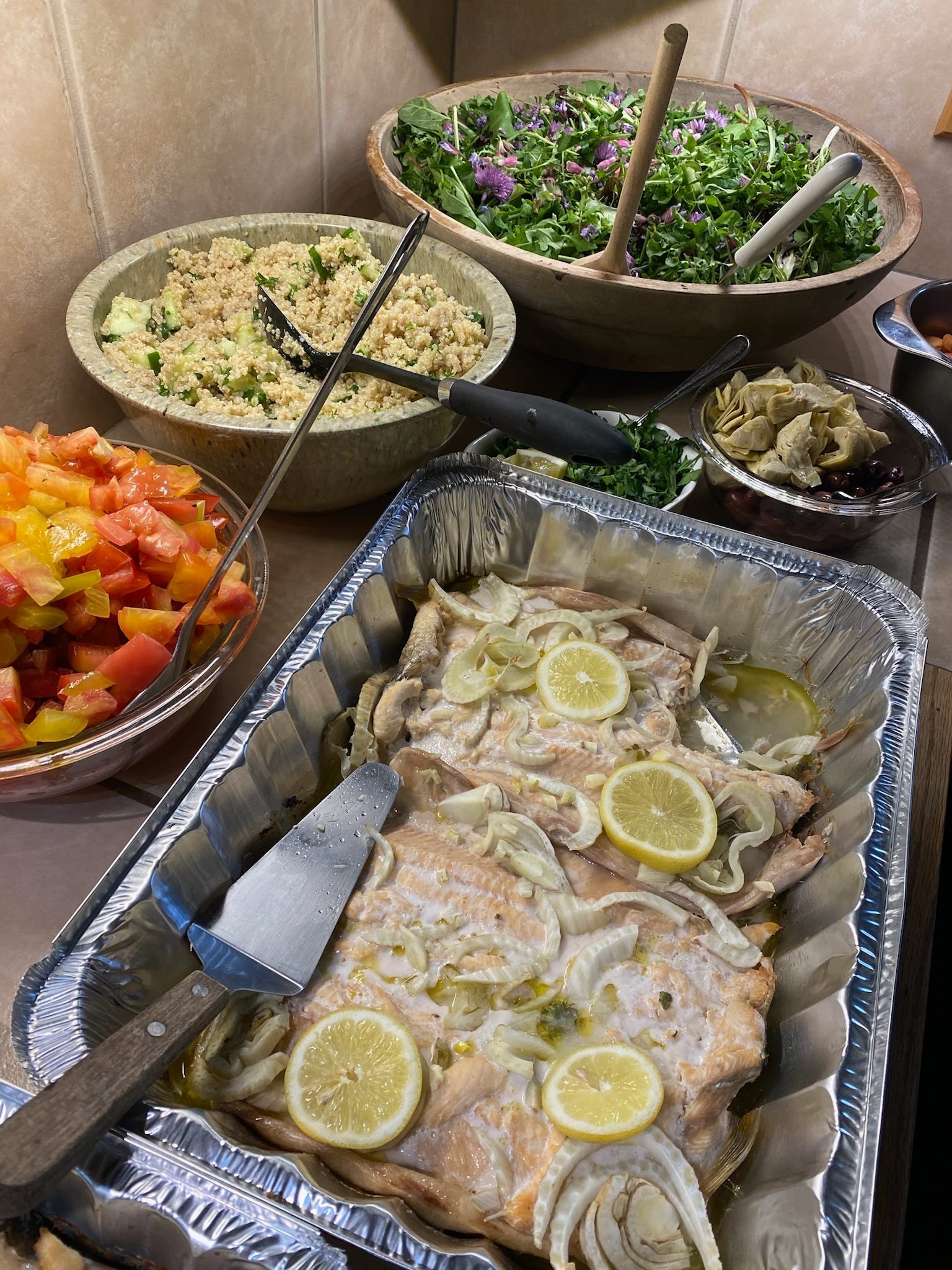 A fully catered retreat spread of roasted fish, grain salad, foraged greens, and tomatoes