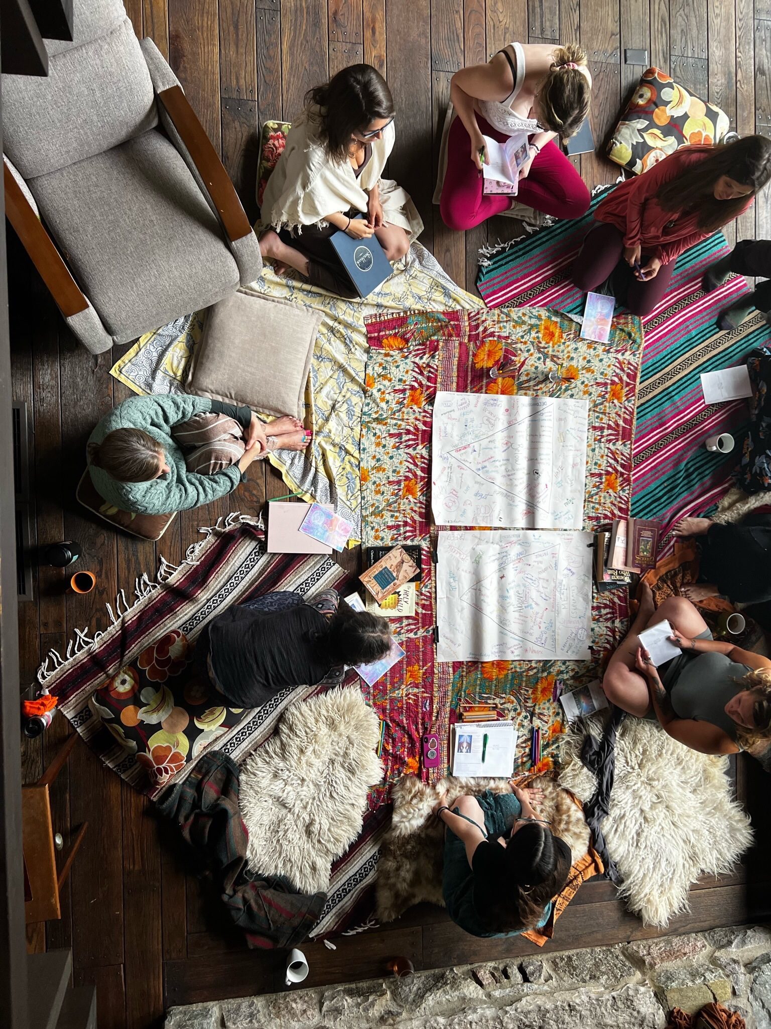 Overhead view of a group gathered in a circle on rugs and sheepskins, working together over large sheets of paper