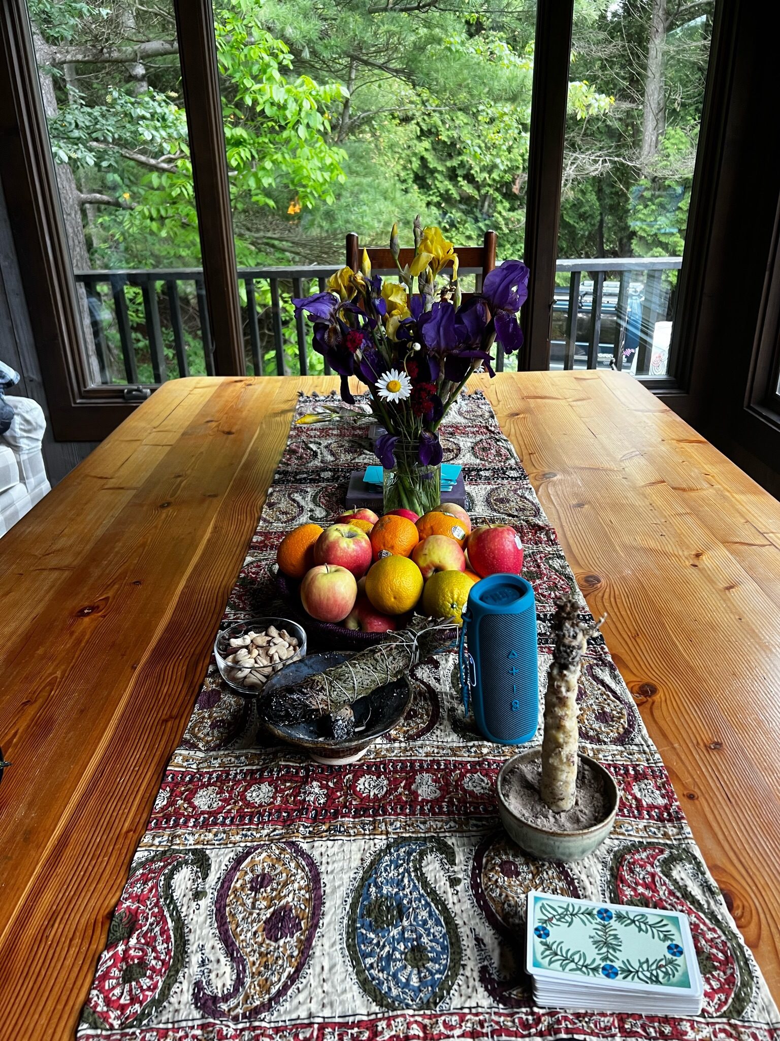 A table set with iris flowers, fresh fruit, a sage bundle, and a tarot deck